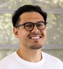 Portrait of a person with short dark hair wearing round glasses and a crew neck shirt